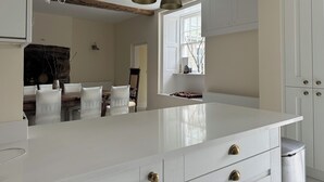 A modern kitchen with a large island, white cabinetry, and pendant lighting. - Cae Nest Hall (llanbedr)