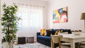 A living room with a sofa, chairs, a dining table, a potted plant, and a colorful abstract painting. - NEW! Belém Riverside 2 bedrooms completely renovated (Lisboa)