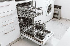 A modern kitchen with a dishwasher, a washing machine, and a trash bin.