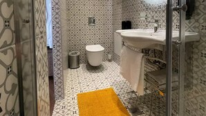 Et badeværelse med mønstret flisegulv, toilet, vask med spejl og en gul løber.