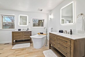 Ein modernes Badezimmer mit zwei Waschbecken, einer freistehenden Badewanne und Holzschränken.