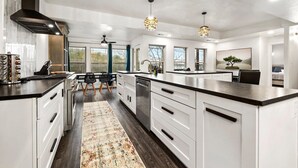 Une cuisine spacieuse avec des meubles blancs, un grand îlot central et des luminaires suspendus.