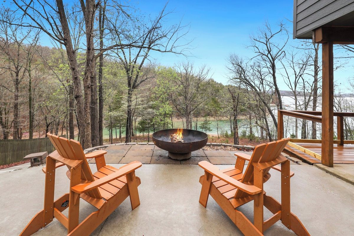 Un espace extérieur aménagé avec deux fauteuils Adirondack en bois, placés face à un foyer, entouré d’une terrasse en béton et offrant une vue sur une zone boisée.