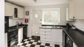 A kitchen with a black and white checkered floor, white cabinets, a stove, a sink, and a window with a diamond pattern. - Magdala (Buxton)