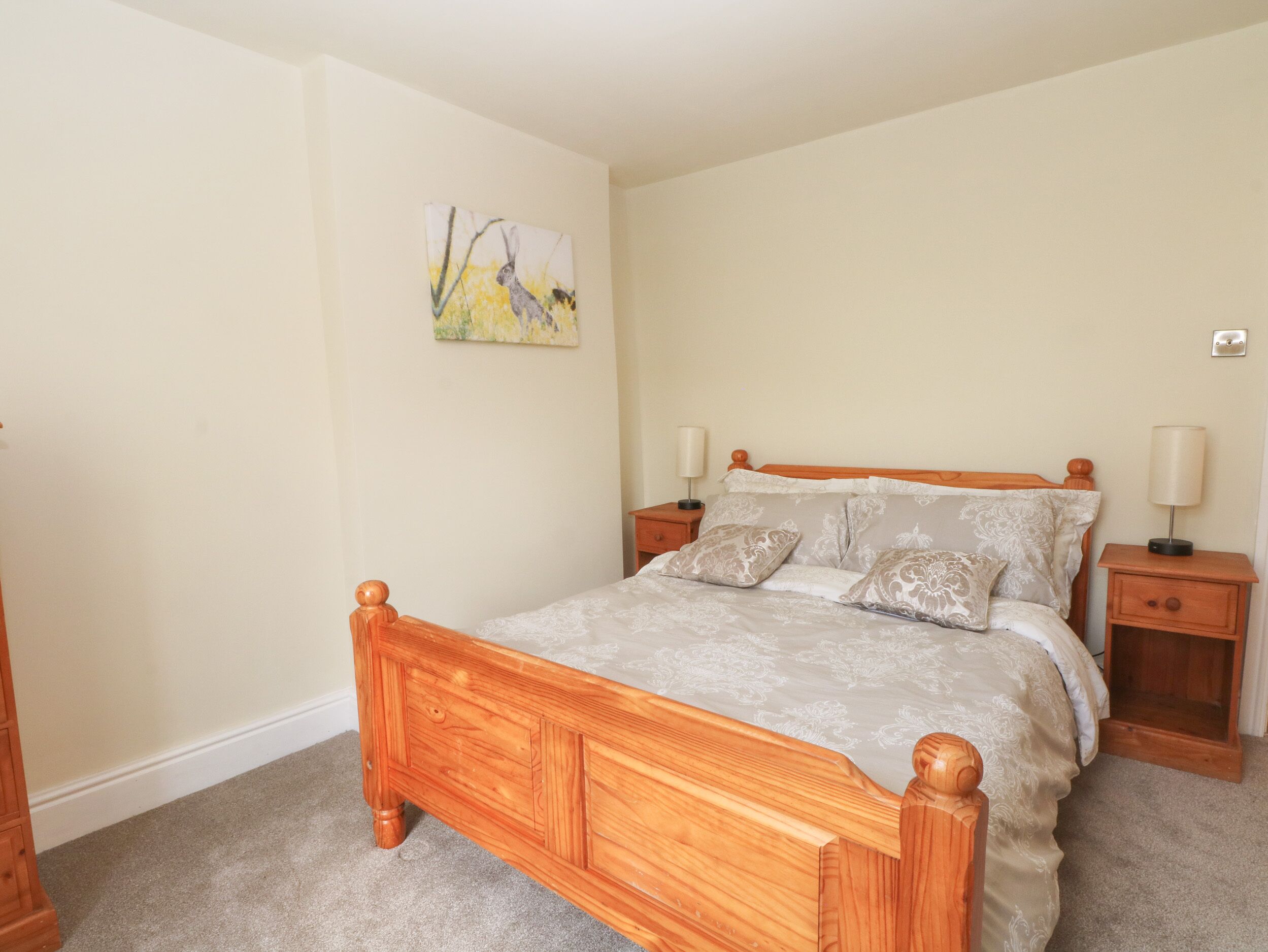A bedroom with a wooden bed, two bedside tables, a nightstand, and a wall-mounted lamp.