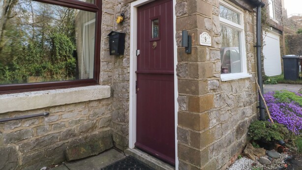 A stone house with a red door, a mailbox, and a number sign indicating the address. - Magdala (Buxton)