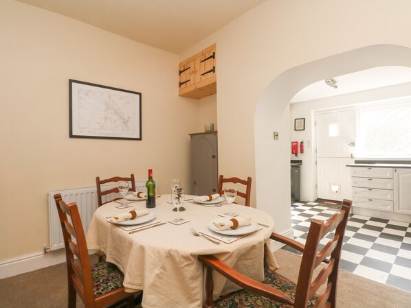 Un coin repas avec une table ronde dressée pour quatre personnes, des chaises en bois, une carte accrochée au mur et une vue sur la cuisine.