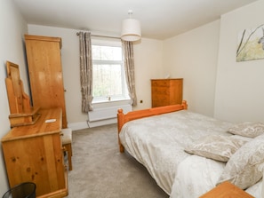 A bedroom with a wooden bed, a wooden dresser, and a window with curtains. - Magdala (Buxton)