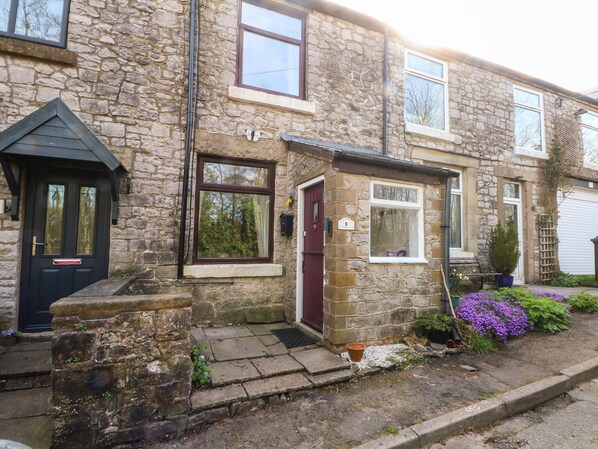 A stone house with a black door, a small porch, and a flower bed with purple flowers. - Magdala (Buxton)