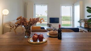 Un comedor moderno con una mesa de madera, un florero con hojas secas, manzanas y una botella de vino.