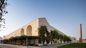 Un edificio con un gran arco central, un patio con pavimento de adoquines y una alta chimenea.