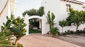 A white building with a tiled roof, a paved entrance, and cacti and other plants in the garden area. - Pleasure of Mecca - Accommodation N4 with kitchen (Zahora)