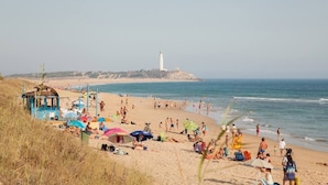 A beach with a lighthouse in the background, people sunbathing, and beach umbrellas. - Pleasure of Mecca - Accommodation N4 with kitchen (Zahora)