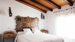 Un dormitorio con una cama grande, un cabecero decorativo en la pared, dos mesitas de noche y una ventana con cortinas.