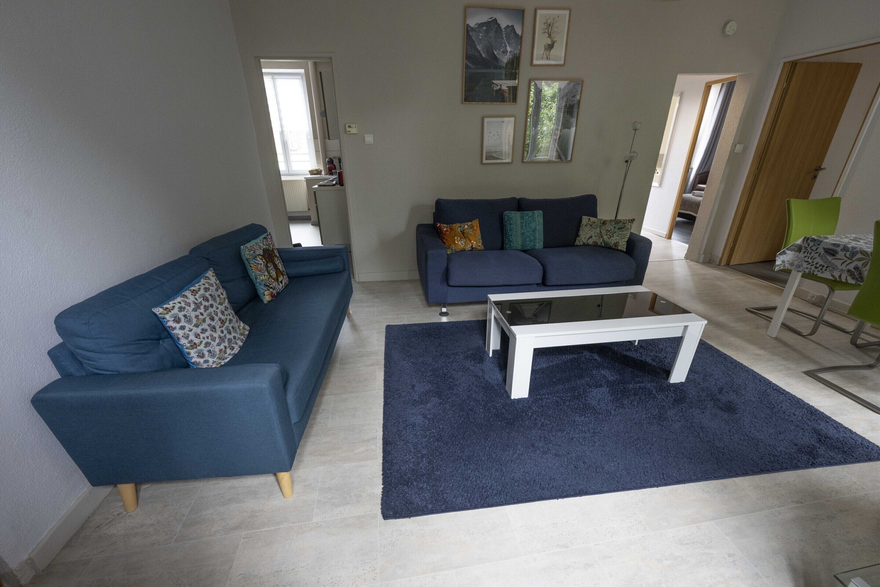 A living room with a blue sofa, a white coffee table, and a dark blue rug.