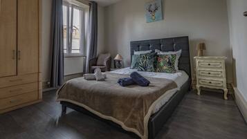 Een slaapkamer met een bed, nachtkastje, stoel, kledingkast en een raam met gordijnen.