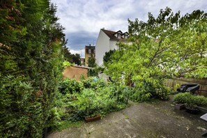 A residential garden with dense foliage, a paved area, and a building with a sloped roof. - i-love-colmar - Les Remparts - Parking (Colmar)
