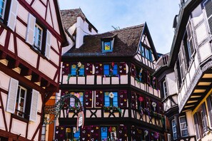 Ein traditionelles Fachwerkhäuschen mit zahlreichen Fenstern, von denen einige mit Fensterläden versehen sind, und einem kleinen Balkon.