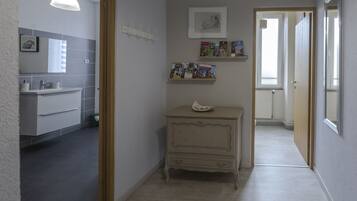 A hallway with a bathroom on the left, a small cabinet with a decorative item, and a door leading to another room.