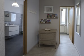 Un pasillo con un baño a la izquierda, un tocador pequeño con espejo y una puerta que da a otra habitación.