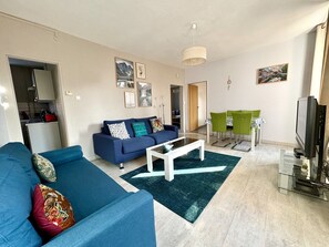 Una sala de estar moderna con un sofá azul, una mesa de centro blanca y un comedor con sillas verdes.