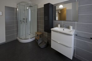 Ein modernes Badezimmer mit einer Duschkabine aus Glas, einem weißen Waschbecken und einem großen Spiegel.