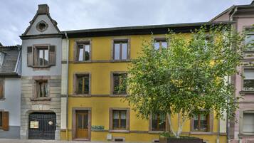 A multi-story building with a yellow facade, a tree in the foreground, and a black gate with mailboxes.