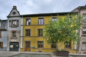 Un edificio de varios pisos con fachada amarilla, una reja negra y un árbol en primer plano.