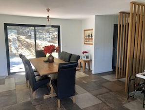 Un espace repas moderne avec une table et des chaises en bois, un vase rempli de fleurs et une vue dégagée grâce à de grandes fenêtres.