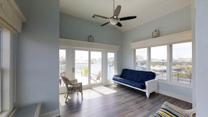 A spacious room with a blue sofa, a chair, and a ceiling fan. Large windows provide a view of the city. - LARGE,Pool,pool table,Arcade,2 Golf Carts,6 Kayaks,free linen,Hot Tub,near beach (Murrells Inlet)