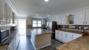 A spacious kitchen with white cabinets, a large island, and a view to the outside. - LARGE,Pool,pool table,Arcade,2 Golf Carts,6 Kayaks,free linen,Hot Tub,near beach (Murrells Inlet)