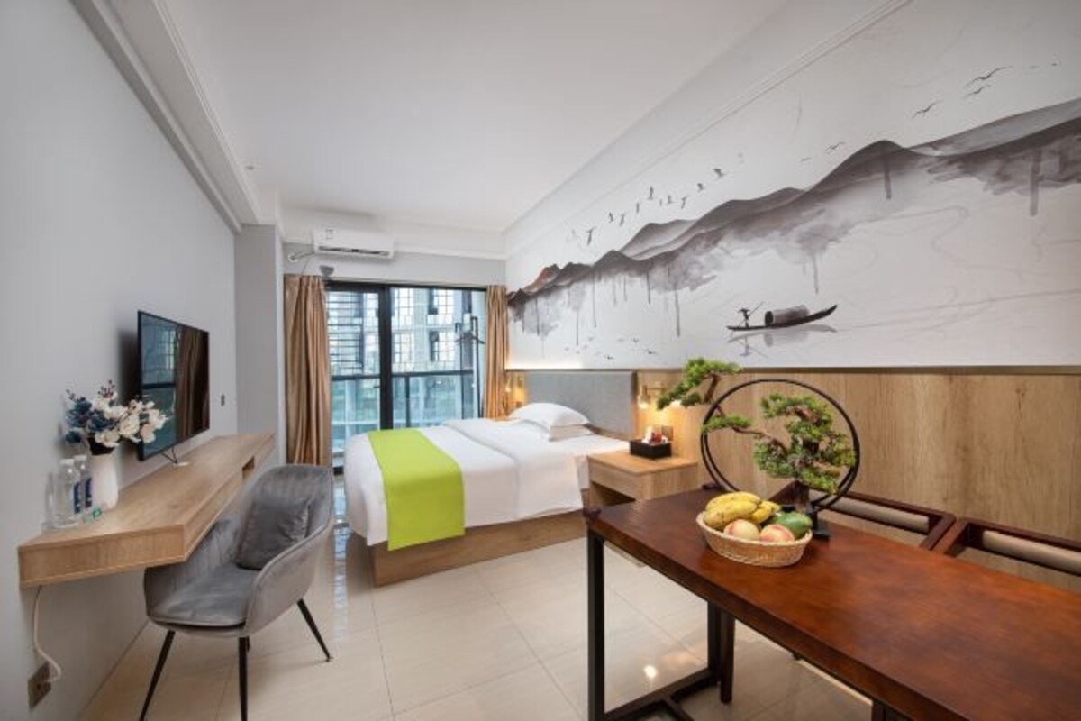 A hotel room with a bed, a desk, a chair, a dining table, and a large wall mural.
