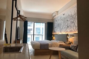 A hotel room with a bed, a small table, a chair, a TV, a window with curtains, and a wall with a tree design. - Light Time Hotel (Nanning Greenland Central Plaza) (Nanning)