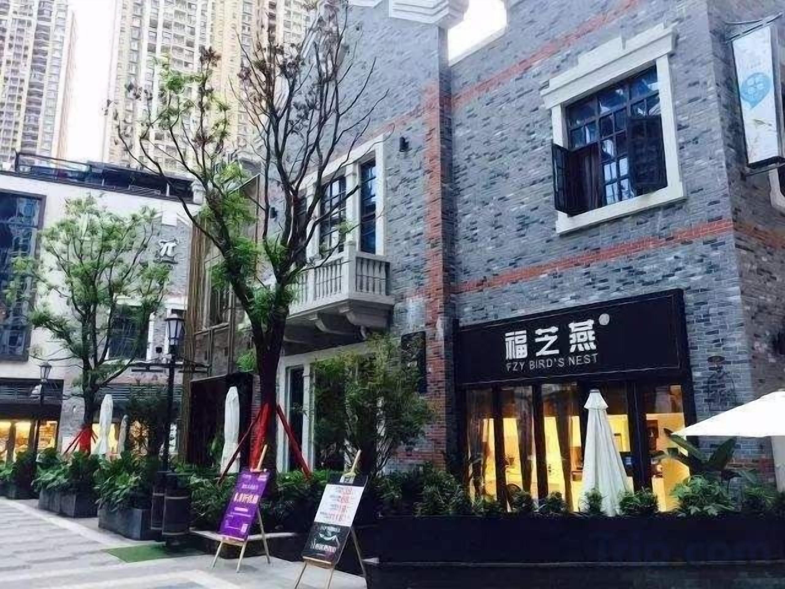 A building with a brick facade, a signboard, and outdoor seating with umbrellas.