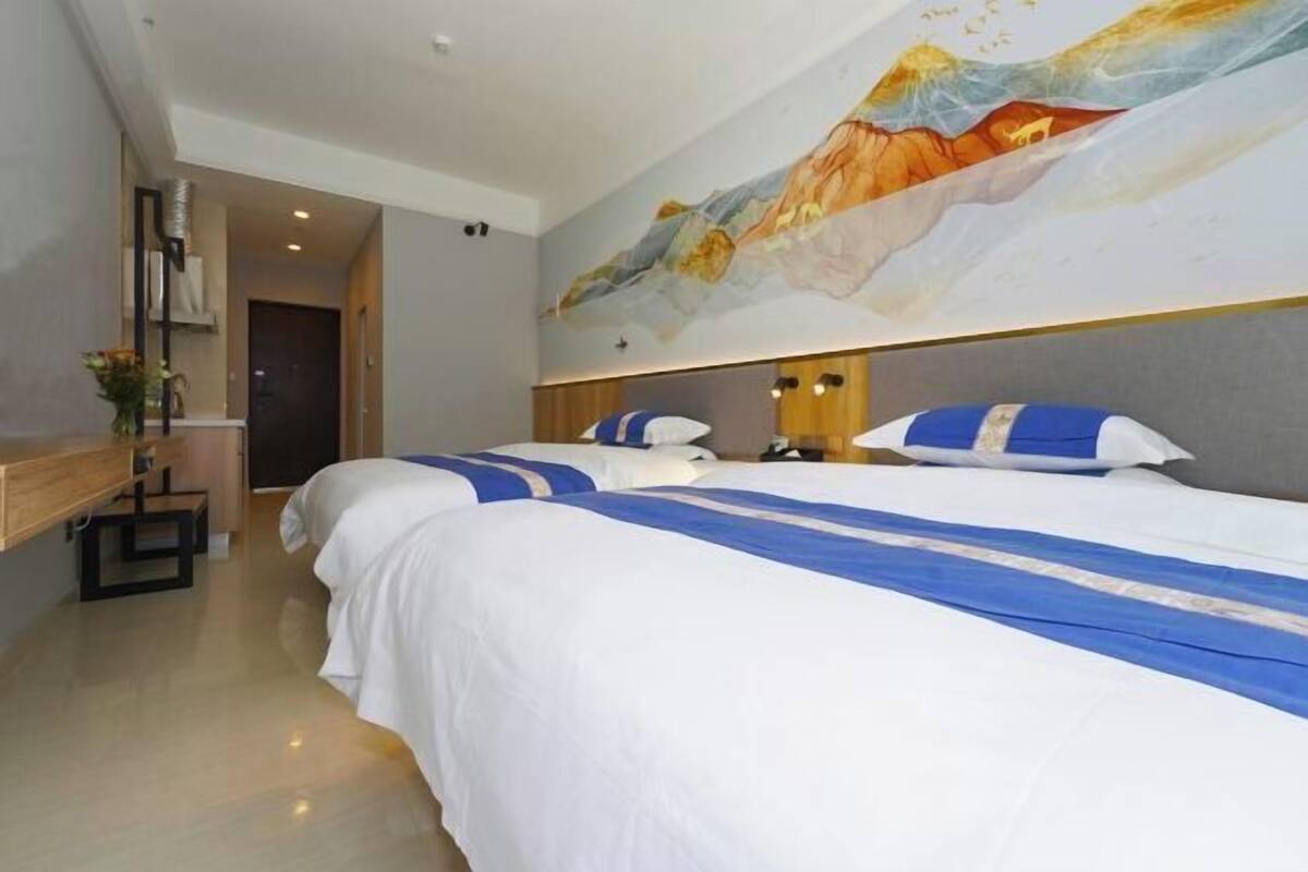 Habitació d'hotel amb dos llits, un quadre gran a la paret i una banca de fusta.