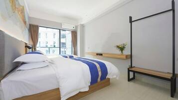 Ein modernes Hotelzimmer mit einem großen Bett, einer Holzbank, einer kleinen Ablage mit einer Vase und Blick auf die Stadt durch das Fenster.