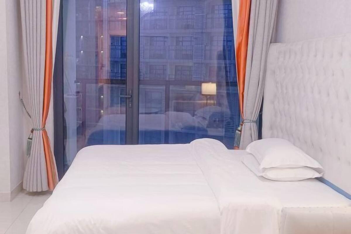 Habitació d'hotel amb un llit, una finestra amb cortines i vistes a edificis a l'exterior.