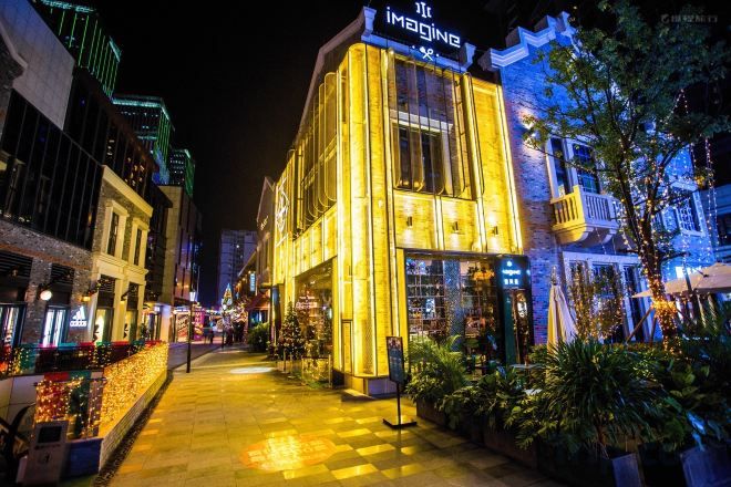 Un hotel bien iluminado con un letrero llamativo, un camino pavimentado y abundante vegetación circundante.