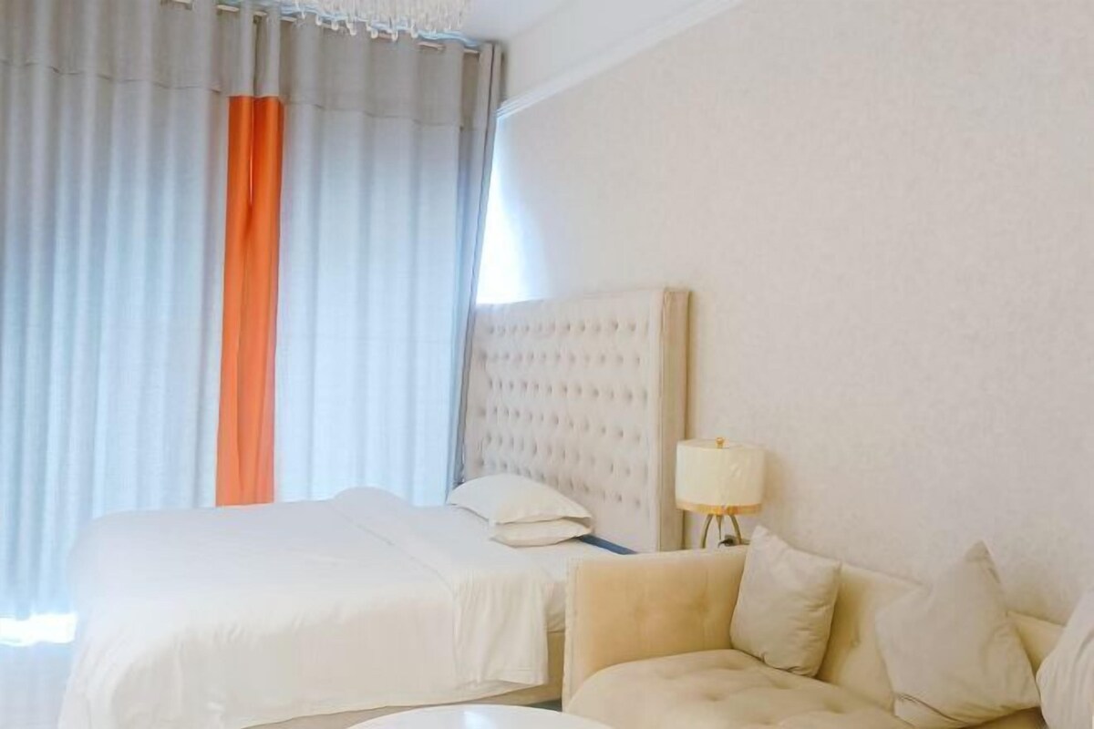 A hotel room with a bed, a sofa, a lamp, and a window with curtains.