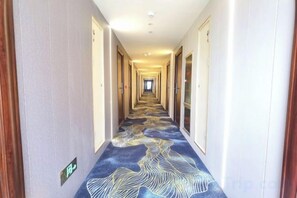 A hotel hallway with carpeted floors, doors on both sides, and a light fixture on the ceiling.