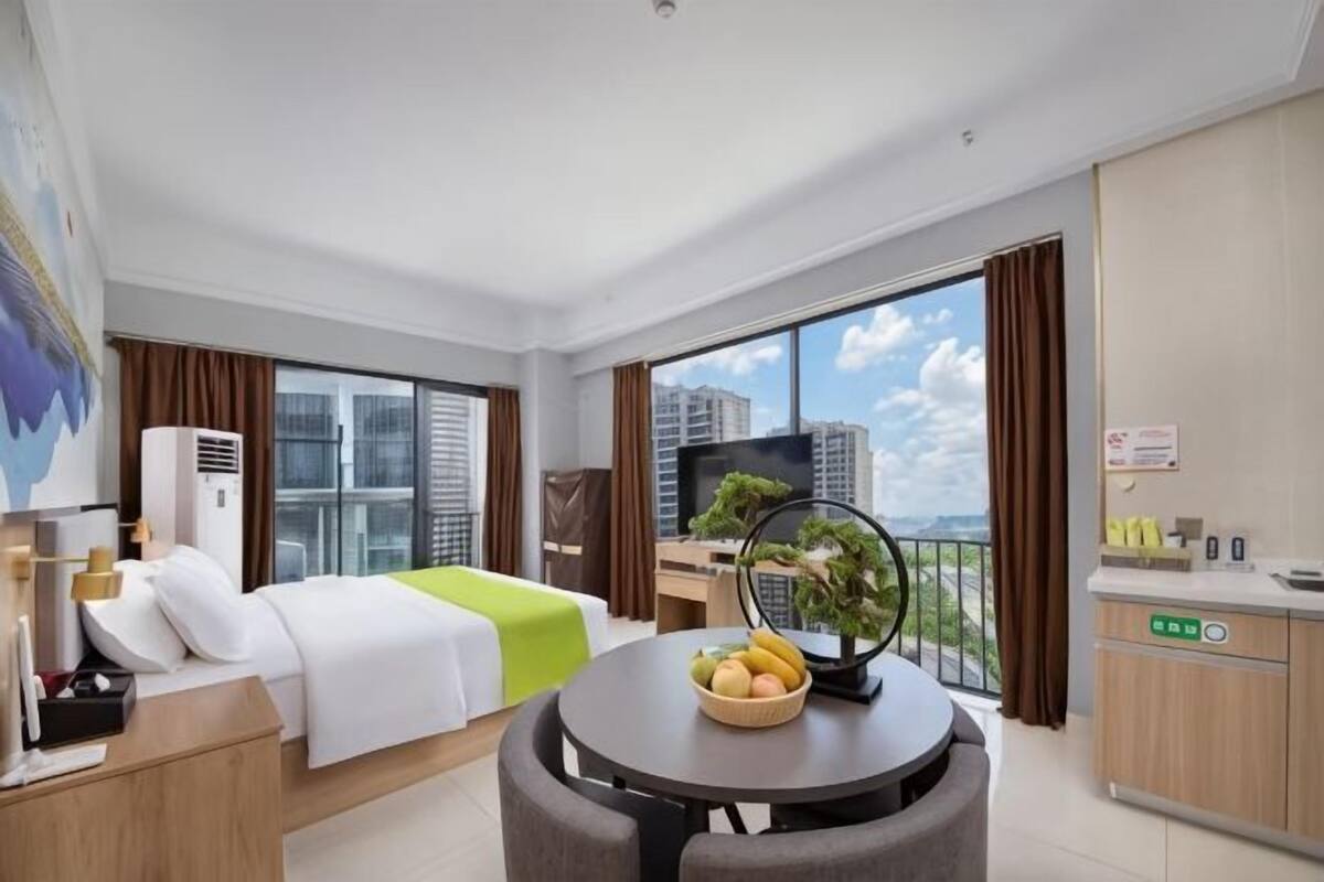 Una habitació d'hotel amb un llit, un escriptori, una taula de menjador, un televisor i vista a la ciutat.