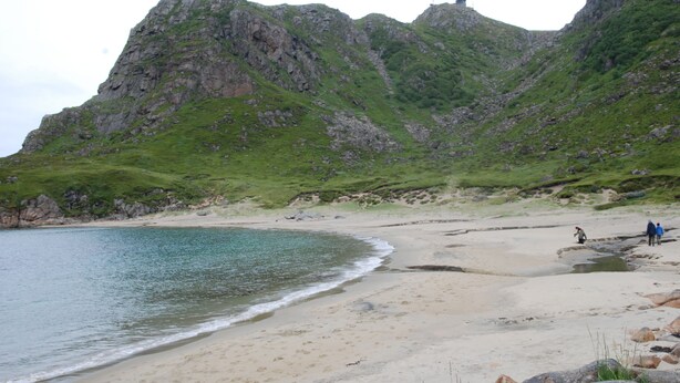 A beach with rocky cliffs and a lighthouse in the background. - Myre Kysthotell (Oksnes)