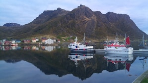 A harbor with boats, a mountain, and buildings along the shore. - Myre Kysthotell (Oksnes)