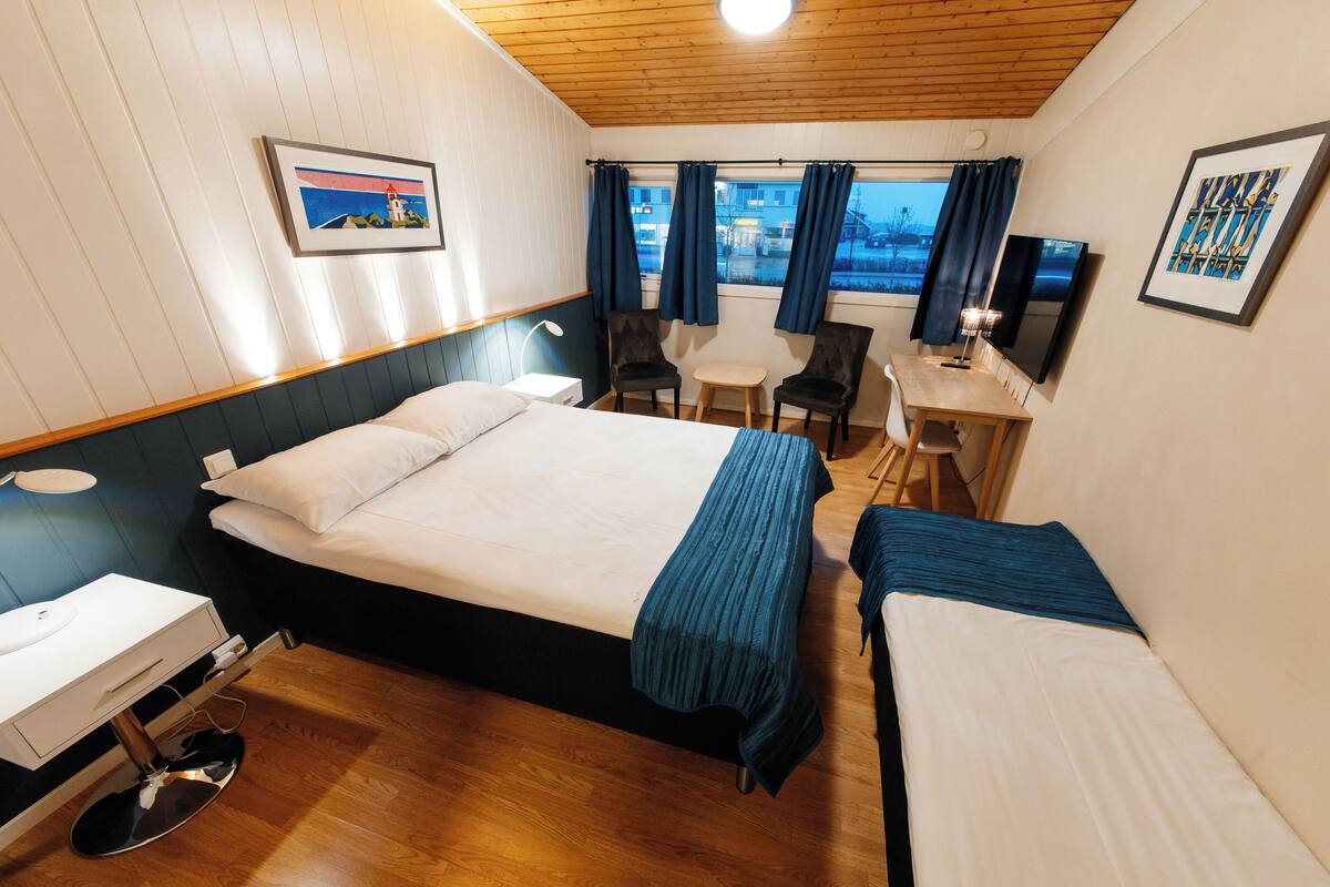 A hotel room with a bed, a desk, two chairs, a TV, and a window with curtains.