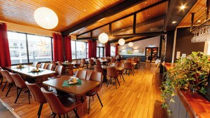 A spacious restaurant with wooden floors and tables, large windows with red curtains, and hanging light fixtures. - Myre Kysthotell (Oksnes)
