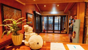 A reception area with a wooden reception desk, a potted plant, and a large painting on the wall. - Myre Kysthotell (Oksnes)