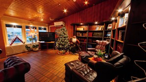 A cozy living room with a wooden ceiling, leather furniture, a Christmas tree, and a bookshelf filled with books. - Myre Kysthotell (Oksnes)