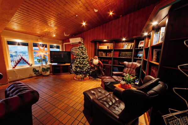 A cozy living room with a wooden ceiling, leather furniture, a Christmas tree, and a bookshelf filled with books.