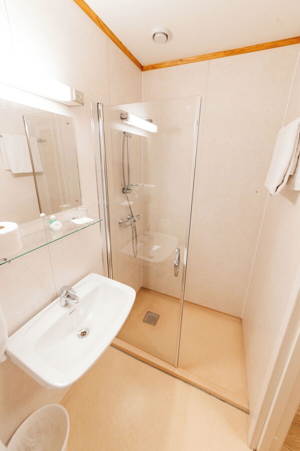 A modern bathroom with a glass-enclosed shower, a white sink, and a mirror above the sink. - Myre Kysthotell (Oksnes)