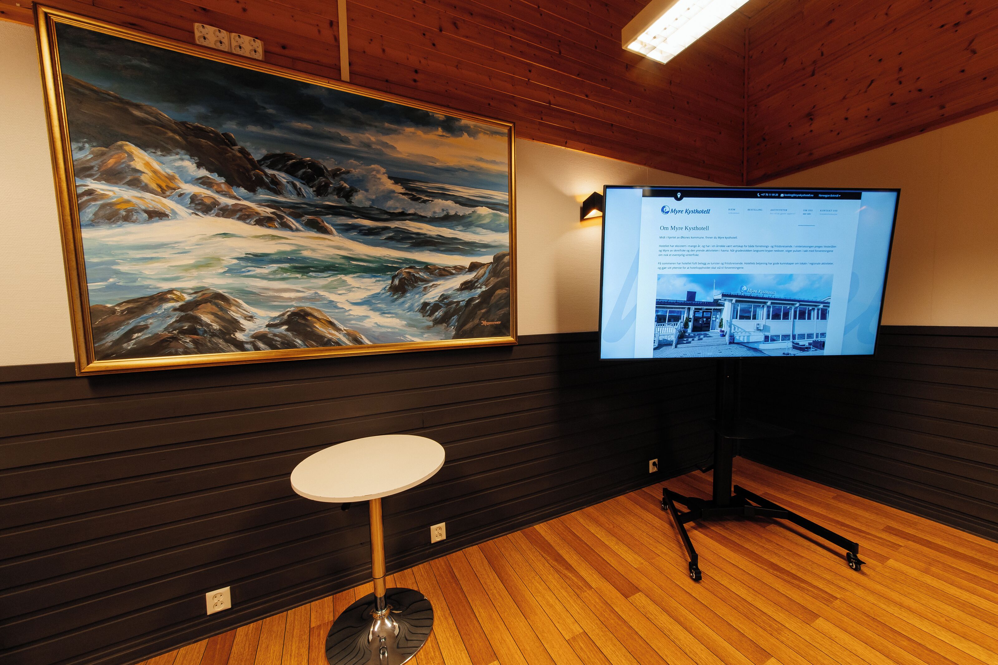 A room with a large framed painting of a seascape, a flat-screen TV, and a round white table.